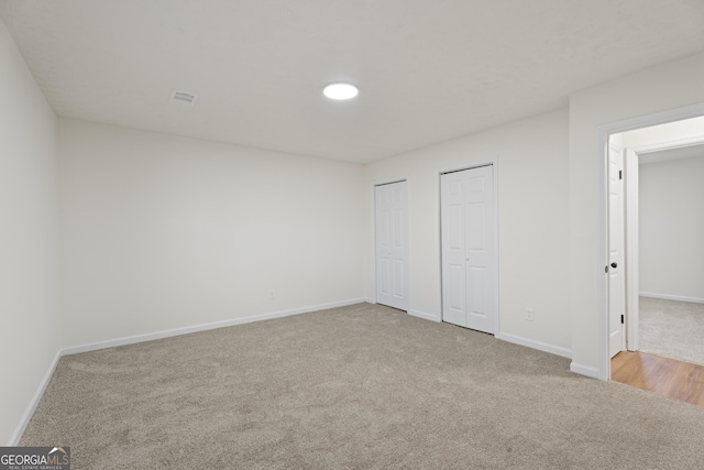 unfurnished bedroom with light carpet, baseboards, and two closets