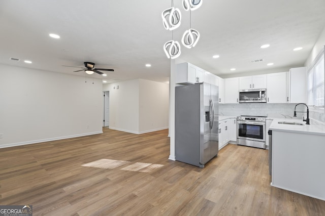kitchen with light countertops, appliances with stainless steel finishes, open floor plan, white cabinets, and a sink