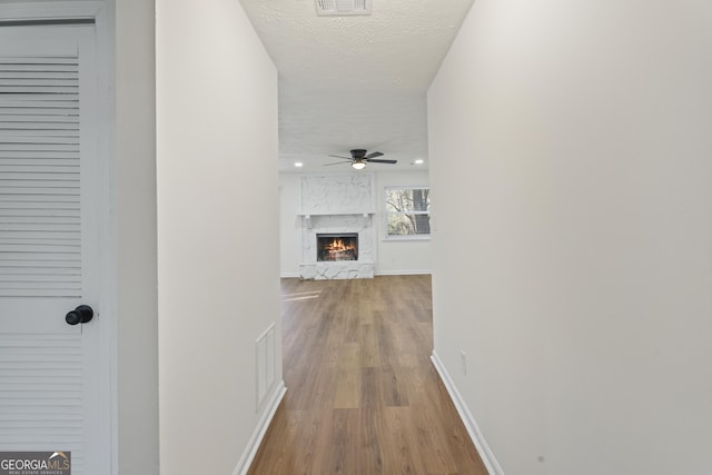 hall featuring a textured ceiling, recessed lighting, wood finished floors, visible vents, and baseboards