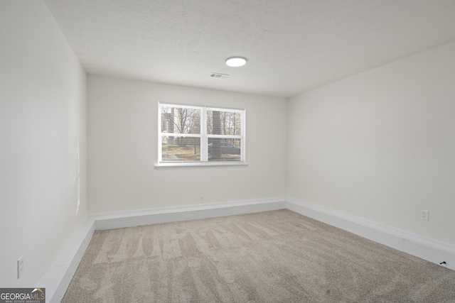 unfurnished room with a textured ceiling, baseboards, visible vents, and light colored carpet
