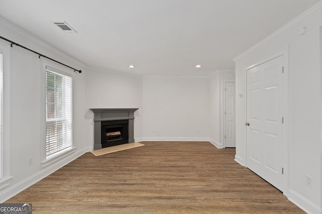 unfurnished living room with crown molding, visible vents, a fireplace with raised hearth, and wood finished floors