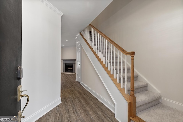 staircase with recessed lighting, a fireplace with raised hearth, baseboards, and wood finished floors