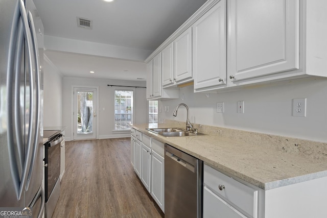 kitchen featuring stainless steel appliances, wood finished floors, white cabinetry, a sink, and light stone countertops