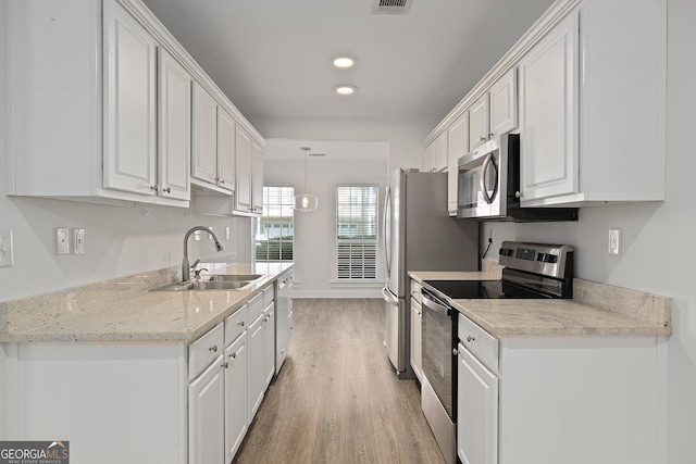 kitchen with light stone counters, appliances with stainless steel finishes, white cabinets, and a sink