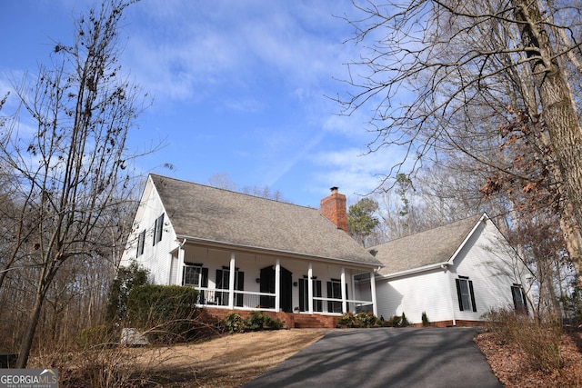 view of front of house with a shingled roof, covered porch, a chimney, and aphalt driveway