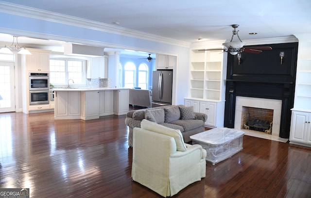 living room featuring a large fireplace, ceiling fan, ornamental molding, and dark wood-type flooring