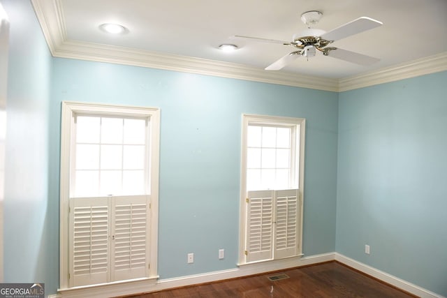 empty room with crown molding, visible vents, a ceiling fan, dark wood-type flooring, and baseboards