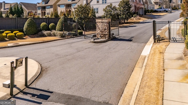 view of road with a gated entry, sidewalks, curbs, a gate, and a residential view