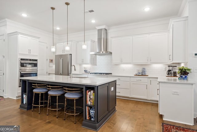 kitchen with stainless steel appliances, a sink, visible vents, white cabinets, and wall chimney range hood