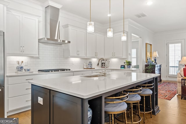 kitchen with visible vents, a kitchen island with sink, wall chimney range hood, gas cooktop, and a sink