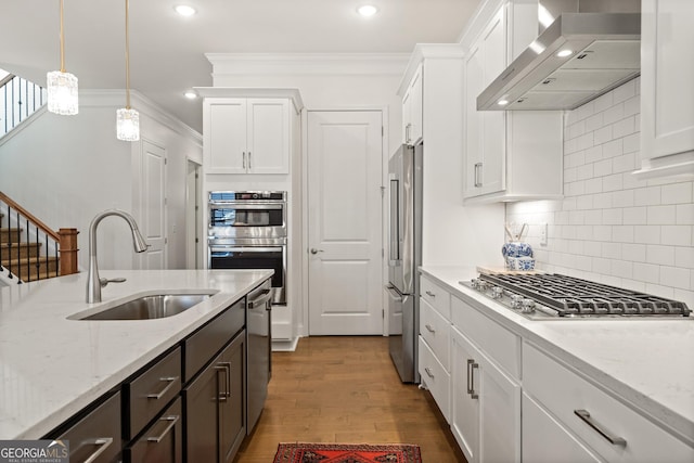 kitchen with crown molding, stainless steel appliances, white cabinetry, a sink, and wall chimney range hood