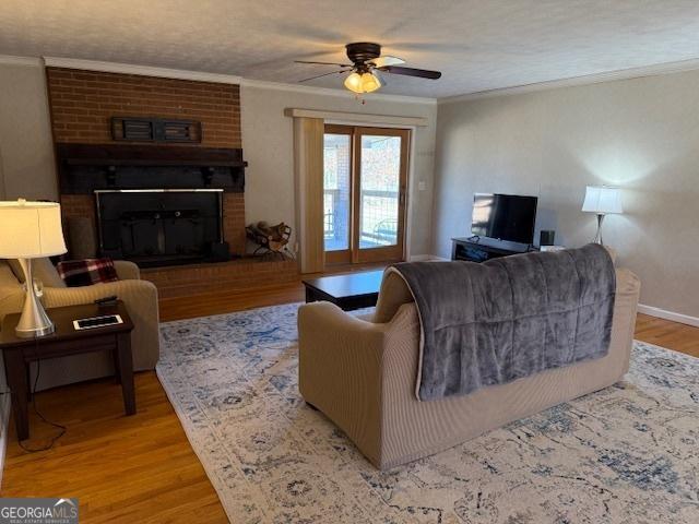 living area featuring a fireplace, crown molding, light wood-style floors, a ceiling fan, and baseboards