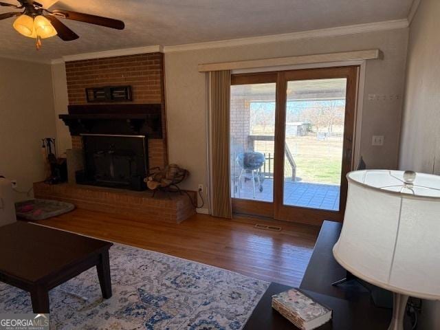 living room with ceiling fan, a fireplace, wood finished floors, and crown molding