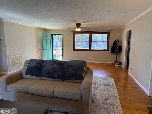 living area featuring a textured ceiling, ornamental molding, wood finished floors, and visible vents