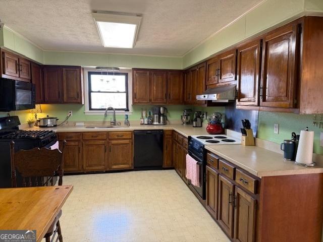 kitchen with light floors, under cabinet range hood, light countertops, black appliances, and a sink