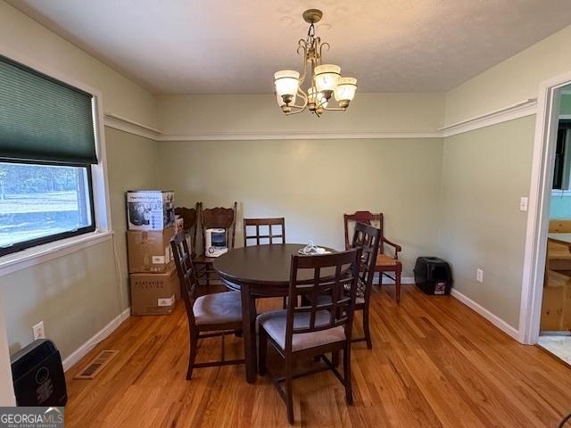 dining room with light wood-type flooring, an inviting chandelier, baseboards, and visible vents