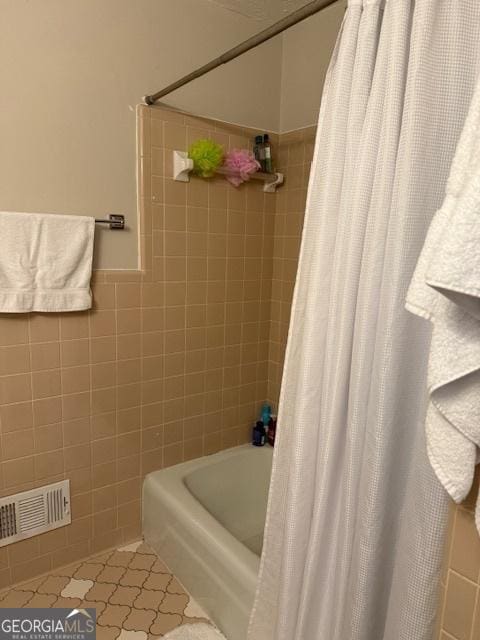 bathroom with a wainscoted wall, tile walls, visible vents, shower / bathtub combination with curtain, and tile patterned flooring