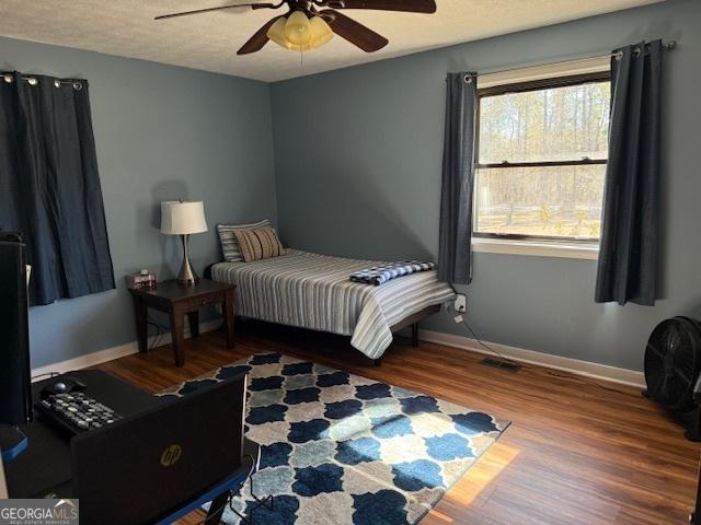 bedroom with a ceiling fan, a textured ceiling, baseboards, and wood finished floors