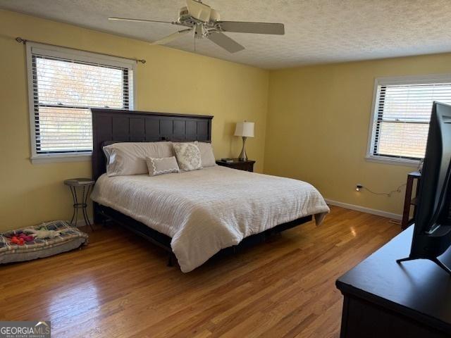 bedroom with ceiling fan, a textured ceiling, baseboards, and wood finished floors