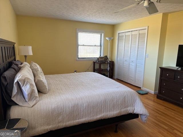 bedroom featuring a textured ceiling, ceiling fan, baseboards, light wood-style floors, and a closet