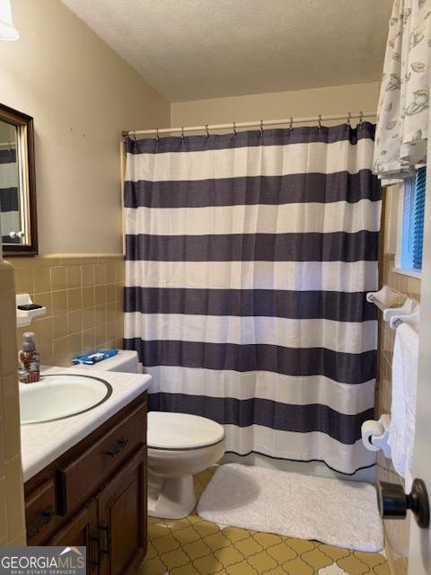 bathroom with wainscoting, toilet, a textured ceiling, vanity, and tile walls