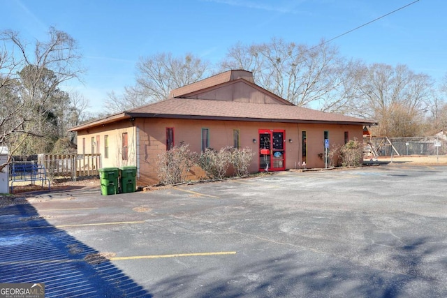 view of side of home featuring a shingled roof, uncovered parking, and fence