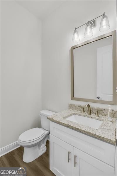 half bath with toilet, wood finished floors, vanity, and baseboards