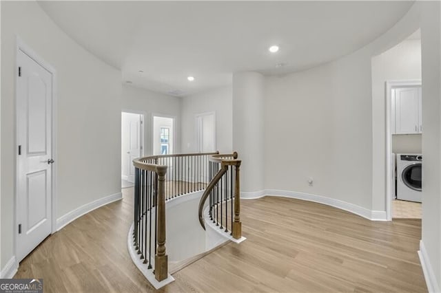 hallway featuring light wood finished floors, washer / dryer, an upstairs landing, and baseboards