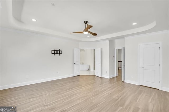 unfurnished bedroom featuring light wood-type flooring, a raised ceiling, crown molding, and baseboards