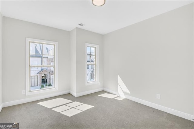 empty room with carpet flooring, visible vents, and baseboards