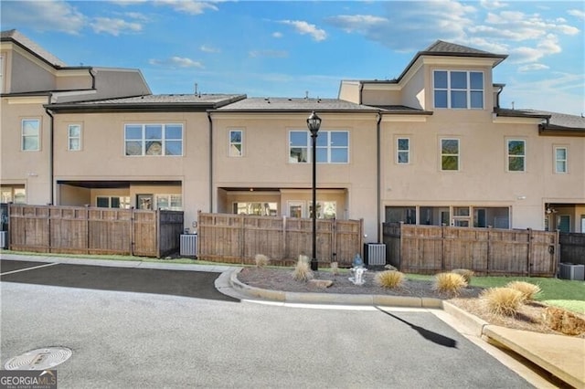 back of house with uncovered parking, a fenced front yard, cooling unit, and stucco siding