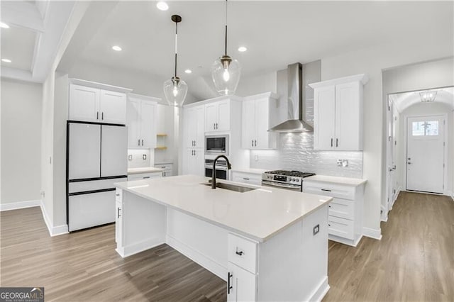 kitchen with wall chimney exhaust hood, refrigerator, built in microwave, stainless steel range with gas cooktop, and a sink