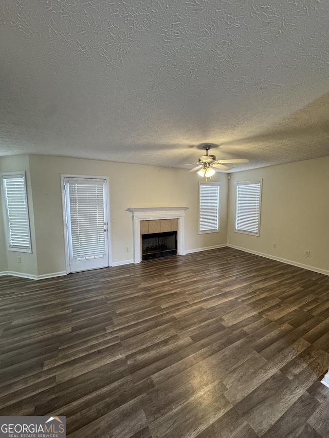 unfurnished living room with baseboards, a ceiling fan, dark wood finished floors, and a tiled fireplace