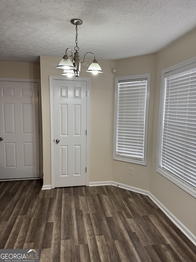 unfurnished dining area featuring a textured ceiling, dark wood-style flooring, a chandelier, and baseboards