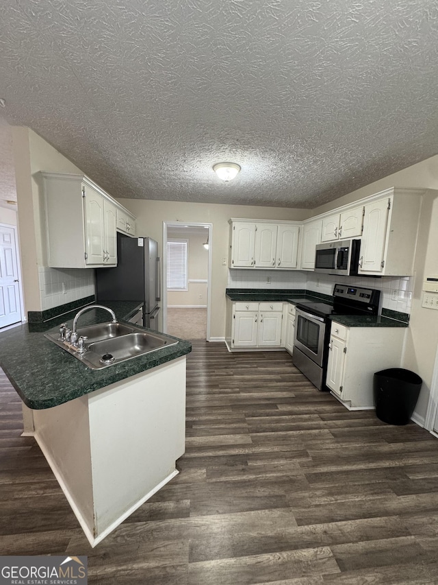 kitchen with appliances with stainless steel finishes, dark countertops, white cabinets, and a peninsula