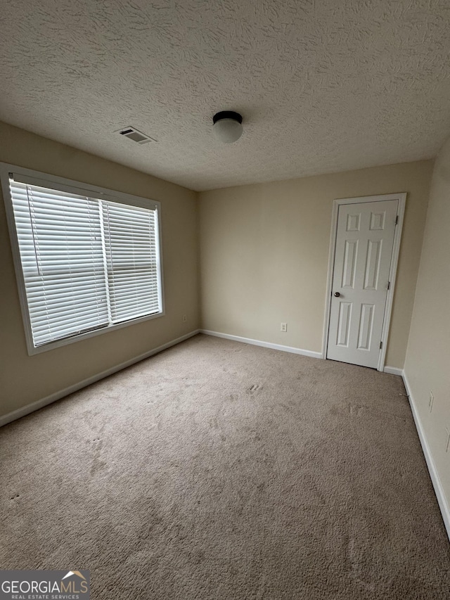 carpeted spare room featuring visible vents, a textured ceiling, and baseboards