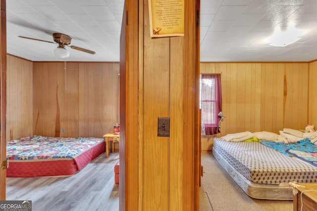 bedroom with crown molding, ceiling fan, wooden walls, and wood finished floors