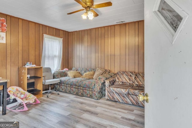 sitting room featuring a ceiling fan, visible vents, wood walls, and light wood finished floors