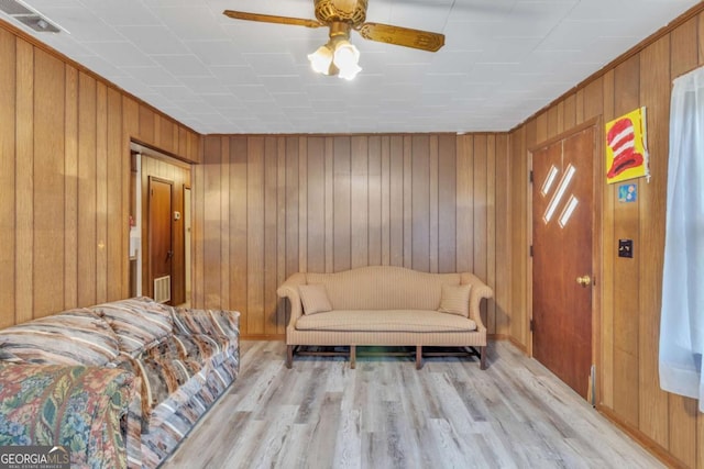 interior space with light wood finished floors, ceiling fan, wooden walls, and visible vents