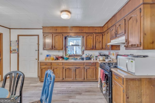 kitchen with light countertops, white microwave, brown cabinetry, gas stove, and under cabinet range hood