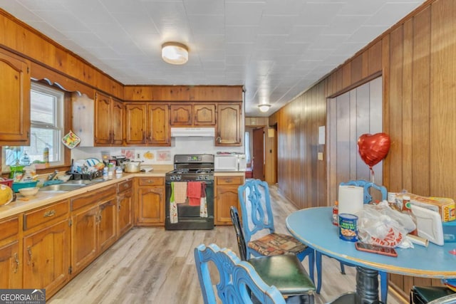 kitchen featuring brown cabinetry, white microwave, light countertops, under cabinet range hood, and gas stove