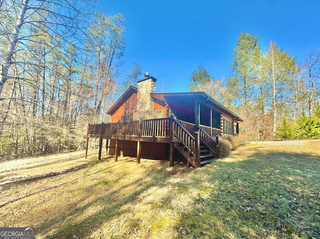 back of property featuring a chimney, a lawn, a deck, and stairs