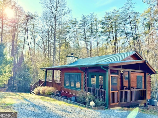 view of front of house with metal roof, log exterior, a chimney, and central air condition unit