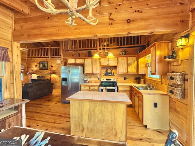 kitchen featuring wooden walls, tile counters, appliances with stainless steel finishes, a center island, and a sink