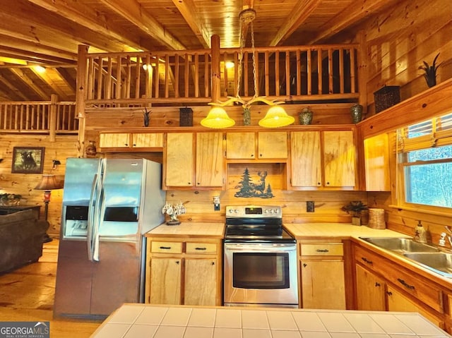 kitchen with wooden walls, tile countertops, appliances with stainless steel finishes, decorative light fixtures, and a sink