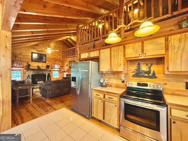 kitchen featuring wooden walls, tile countertops, open floor plan, stainless steel appliances, and a stone fireplace