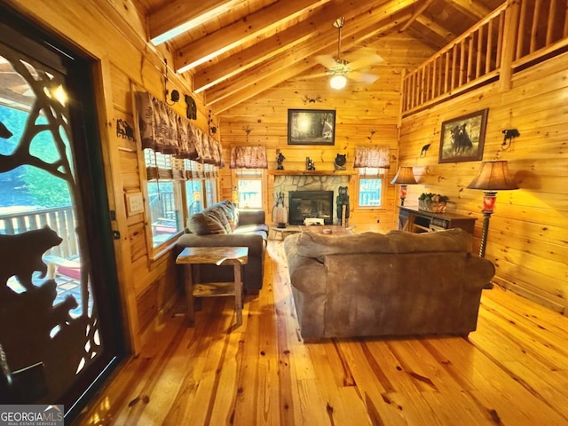 living room featuring wooden walls, a fireplace, wood finished floors, a ceiling fan, and beamed ceiling