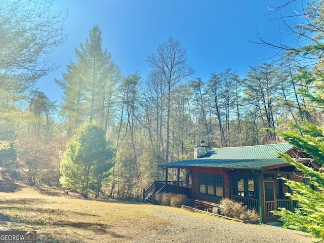 view of side of home with a porch, a yard, metal roof, and a chimney