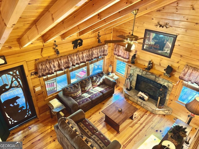 living room with a stone fireplace, wood walls, lofted ceiling with beams, and wood finished floors