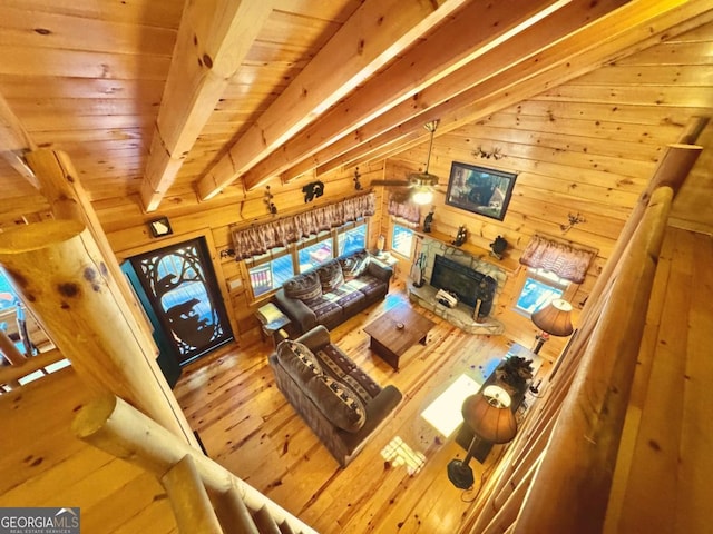 living area with wooden walls, wooden ceiling, wood finished floors, vaulted ceiling with beams, and a stone fireplace